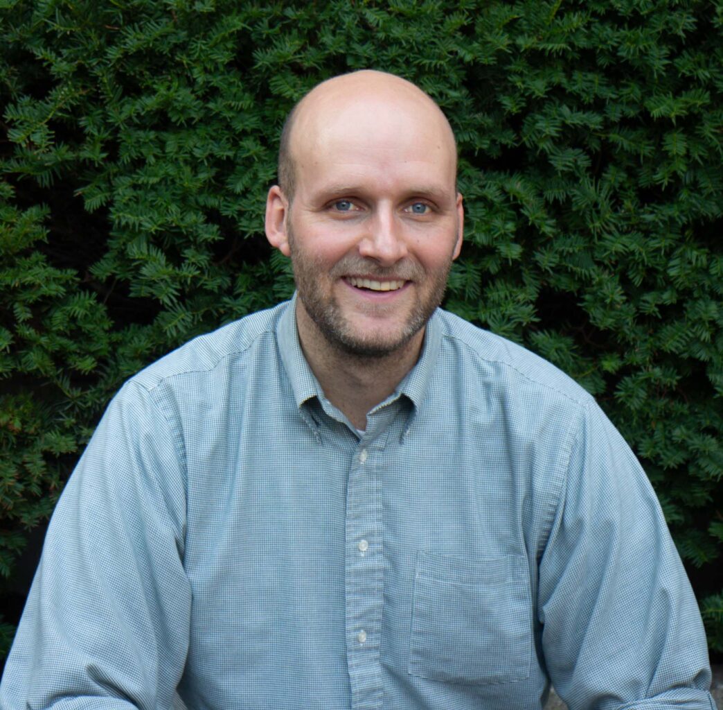 A bald man in a blue shirt sitting on a bench.