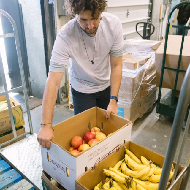 A man unloading boxes of apples and bananas donated to Boston area food recovery charity Lovin Spoonfuls.