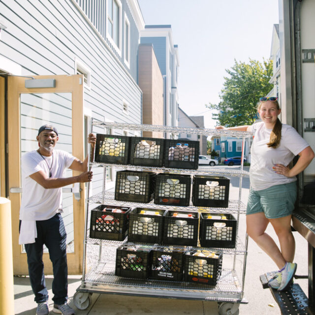 Two people standing in front of a moving truck with crates of food donated to Boston area food recovery organization Lovin Spoonfuls.