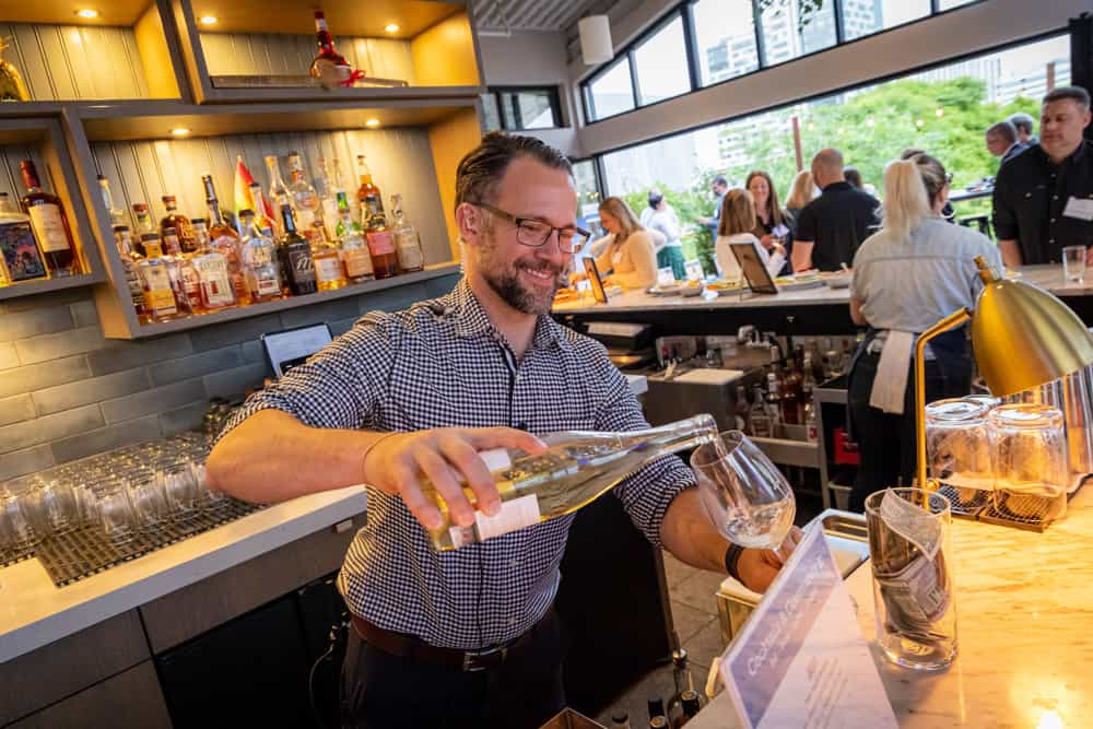 A man pouring a glass of wine at a bar at the Cocktails and Community event hosted by Boston area food recovery organization Lovin Spoonfuls.