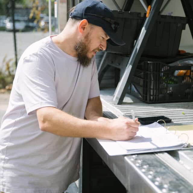 A man writing on a piece of paper in front of a moving truck while working for Boston area food recovery organization Lovin Spoonfuls.