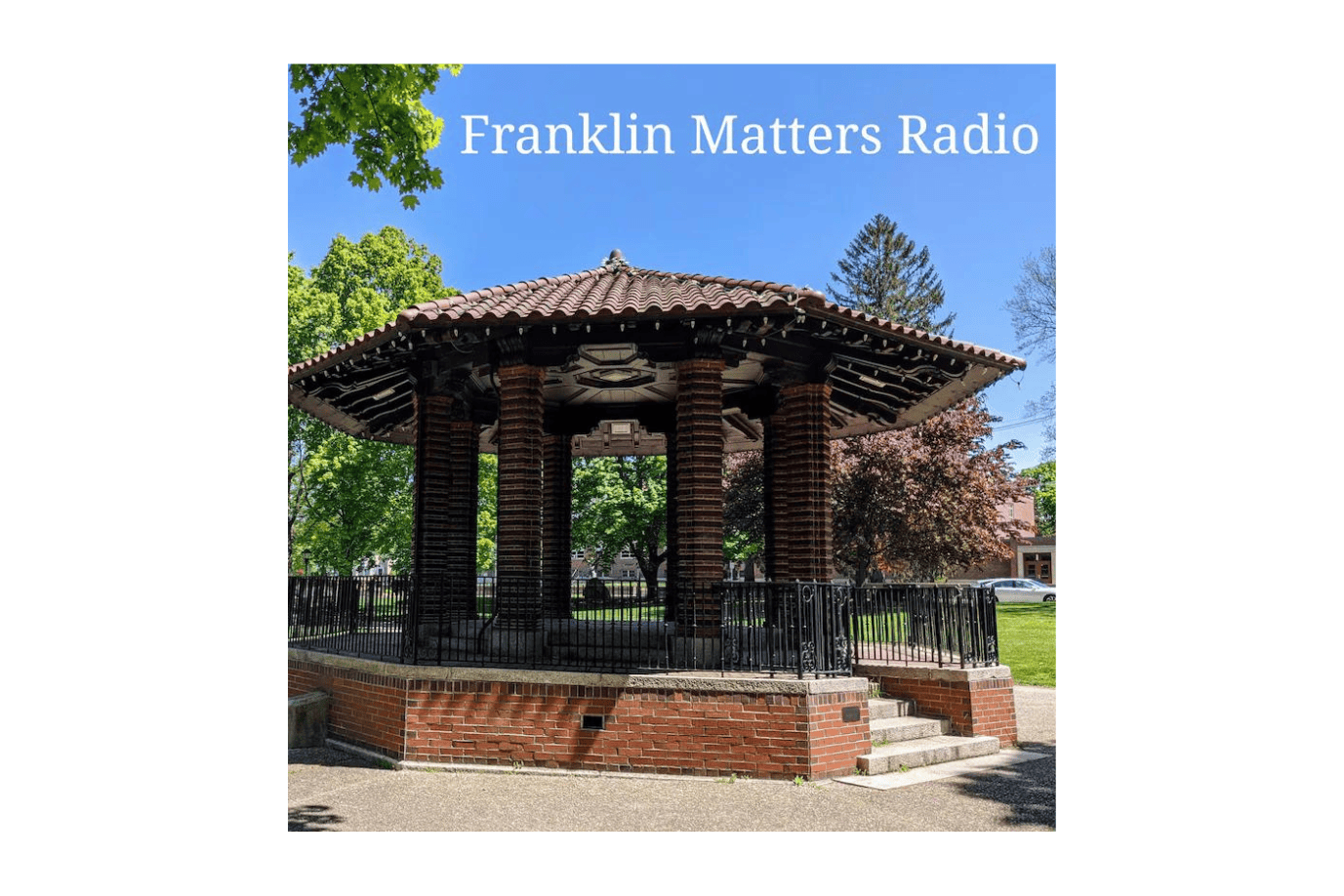 A brick gazebo with a tiled roof stands in a park, surrounded by green trees and a clear blue sky. Text at the top reads "Franklin Matters Radio.