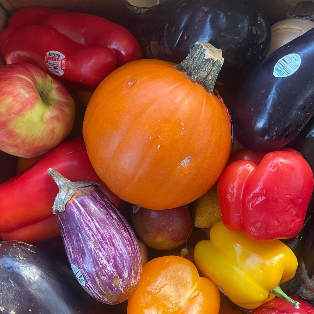 A variety of colorful fruits and vegetables, including a pumpkin, apples, peppers, and eggplants, arranged closely together.