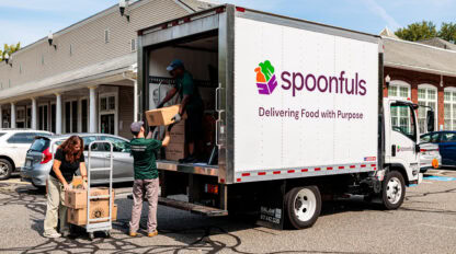 People loading boxes into a "spoonfuls" delivery truck parked outside a building.