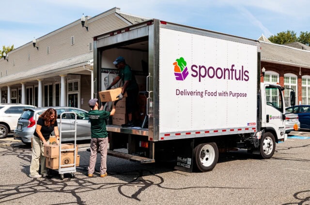 People loading boxes into a "spoonfuls" delivery truck parked outside a building.