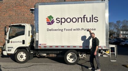 A man stands beside a Spoonfuls delivery truck with the slogan "Delivering Food with Purpose" on the side.