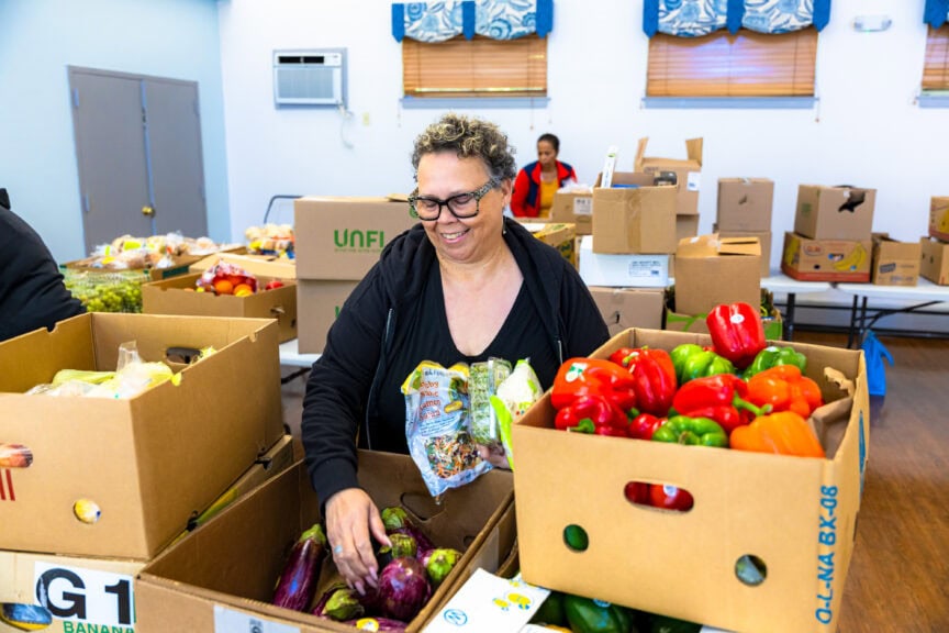A community partner smiles as she sorts through recovered produce delivered by Spoonfuls to demonstrate the impact of food recovery on food assistance programs.