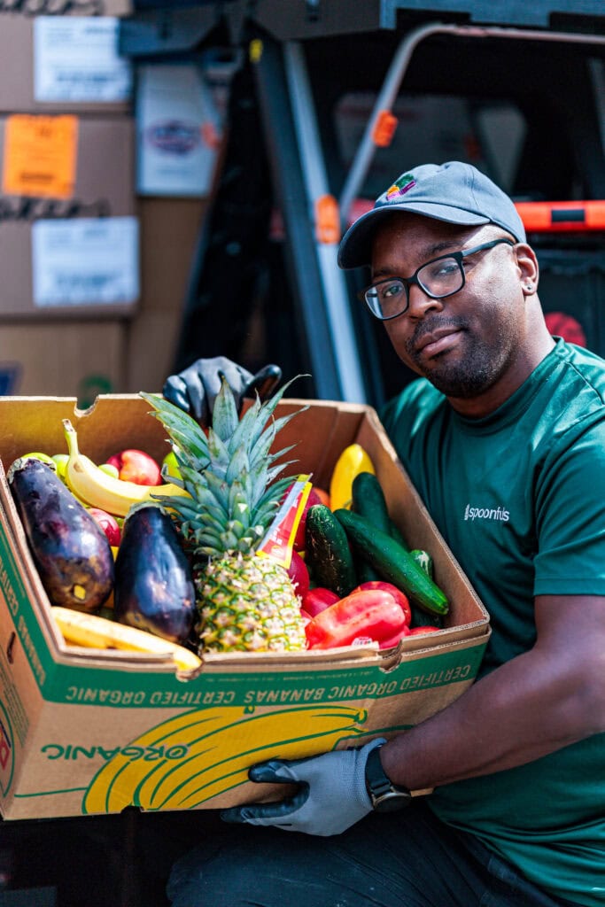A Spoonfuls staff member posing with a box of fresh, healthy produce to illustrate how our team is a part of our story.