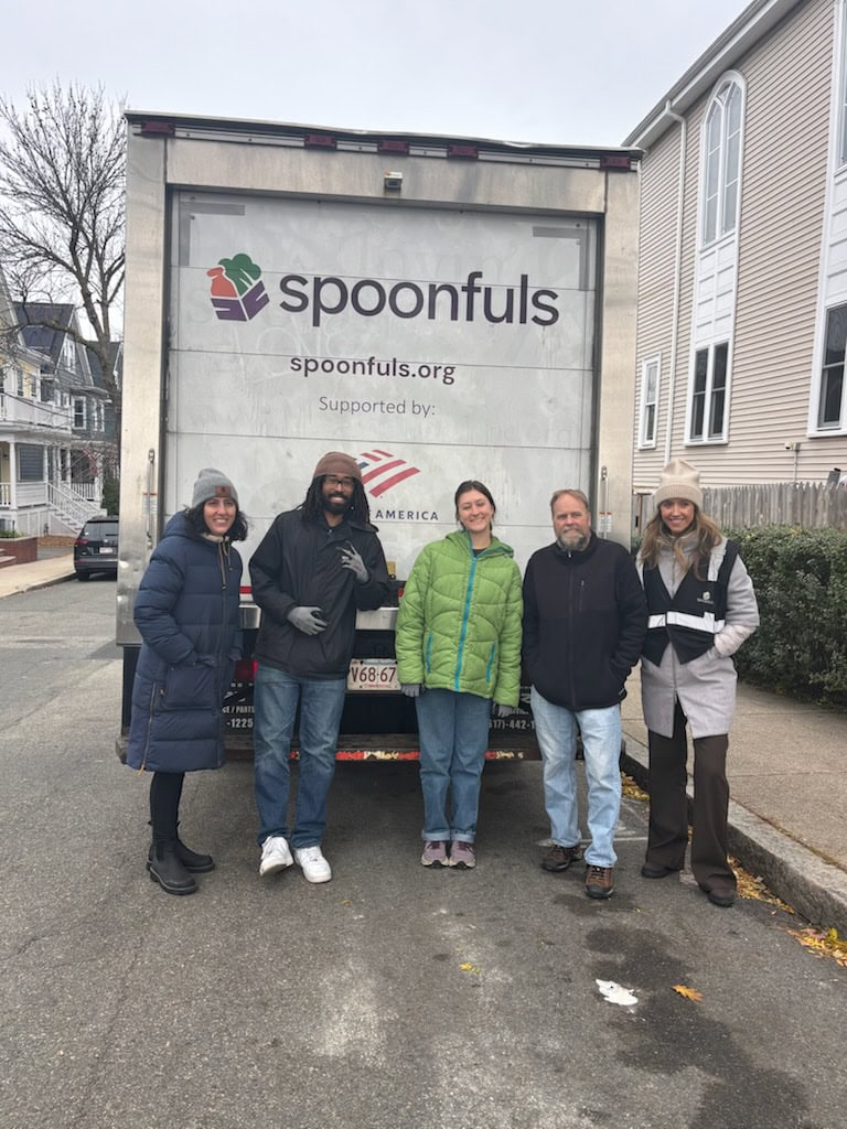 Five people stand in front of a Spoonfuls truck parked on a residential street, posing for a group photo on a cloudy day.