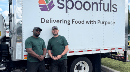 Two employees in branded green t-shirts stand in front of a white box truck with the “Spoonfuls” logo and the text “Delivering Food with Purpose.”