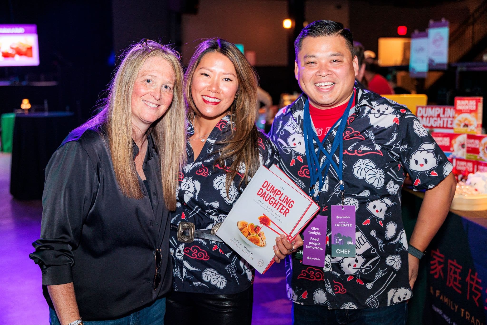 Three people smiling and posing for a photo, with the person in the center holding a copy of “The Dumpling Daughter” cookbook.
