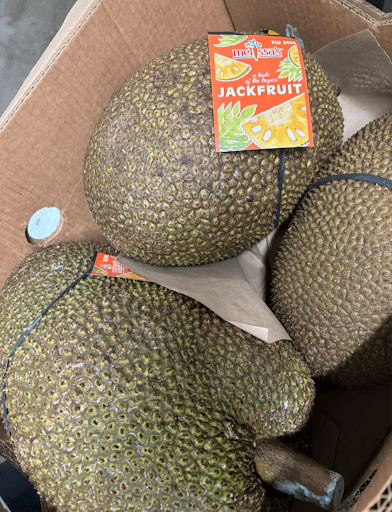 Three large, spiky jackfruits in a cardboard shipping crate, with a Melissa’s brand label attached to one.